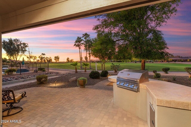 patio terrace at dusk featuring exterior kitchen, a grill, and a lawn