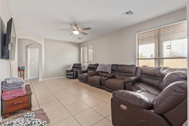 living room with arched walkways, ceiling fan, light tile patterned flooring, and baseboards