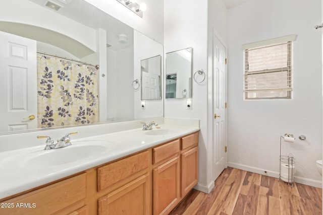 bathroom with wood finished floors, toilet, double vanity, and baseboards