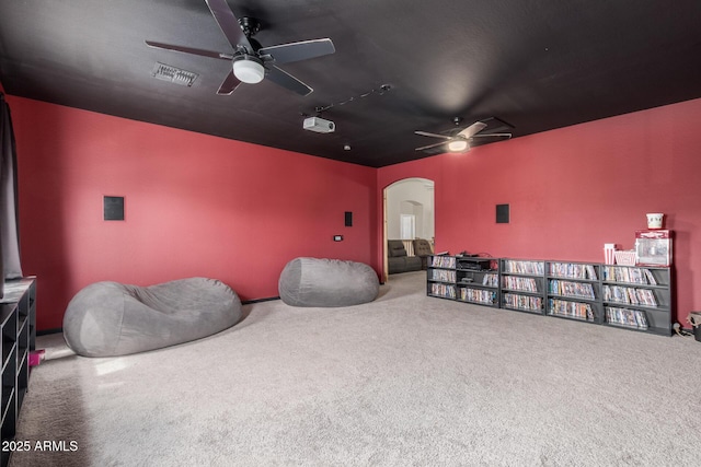 carpeted cinema room with ceiling fan and arched walkways