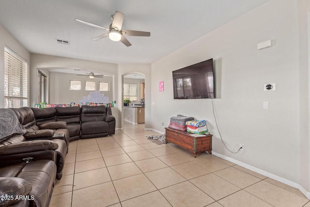 living room featuring arched walkways, ceiling fan, light tile patterned flooring, and baseboards