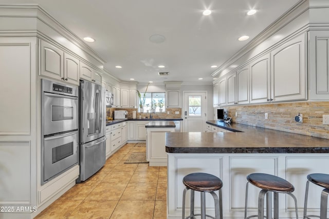 kitchen with kitchen peninsula, white cabinets, a kitchen breakfast bar, and appliances with stainless steel finishes