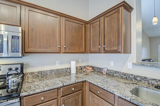 kitchen featuring a sink, light stone counters, stainless steel appliances, brown cabinetry, and hanging light fixtures