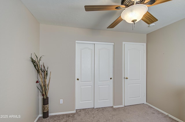 unfurnished bedroom featuring a closet, light colored carpet, a ceiling fan, and baseboards