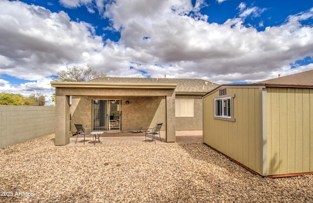 back of property featuring fence, roof with shingles, a storage shed, an outdoor structure, and a patio area