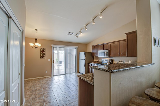 kitchen with visible vents, vaulted ceiling, dark stone countertops, a peninsula, and stainless steel appliances