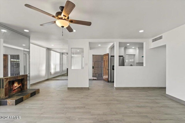 unfurnished living room featuring ceiling fan and a tiled fireplace