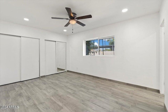 unfurnished bedroom featuring light hardwood / wood-style floors, ceiling fan, and multiple closets