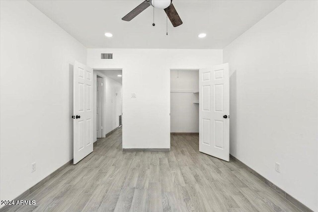 unfurnished bedroom with a closet, light hardwood / wood-style floors, a spacious closet, and ceiling fan