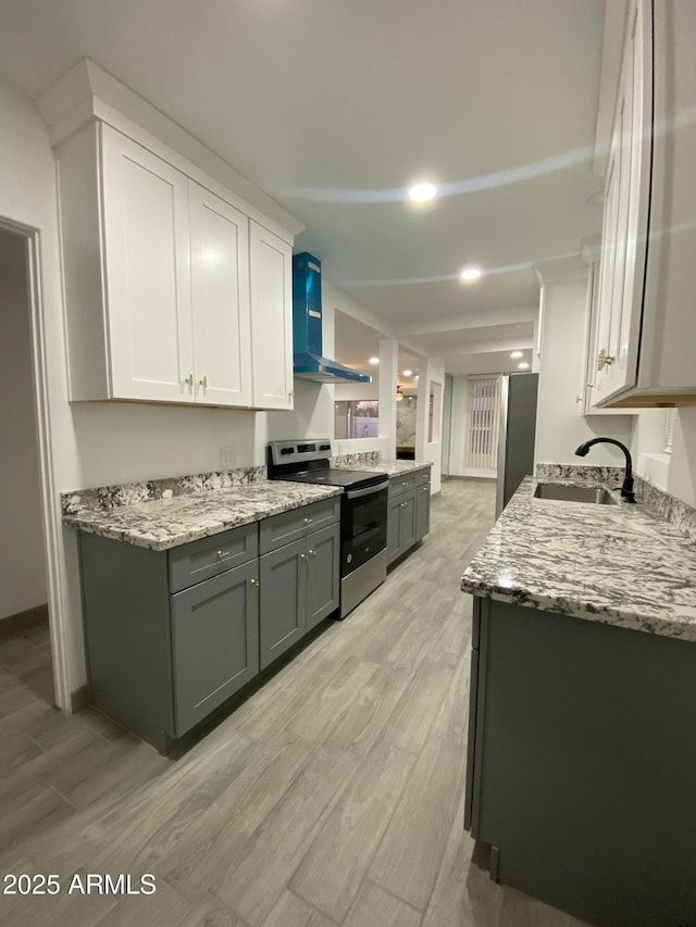 kitchen with stainless steel electric range, light wood finished floors, white cabinets, a sink, and wall chimney exhaust hood