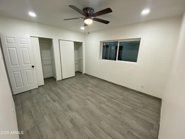 unfurnished bedroom with ceiling fan, multiple closets, wood finished floors, and recessed lighting