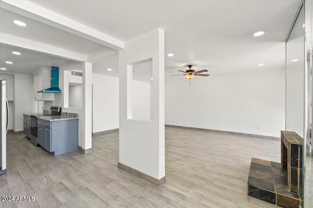 kitchen featuring a ceiling fan, wall chimney exhaust hood, open floor plan, stainless steel electric range, and light wood-type flooring