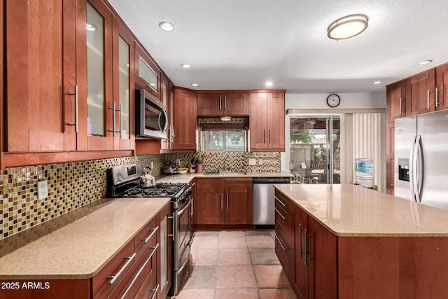 kitchen featuring appliances with stainless steel finishes, light stone counters, a sink, a center island, and glass insert cabinets