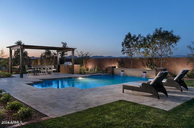 pool at dusk featuring pool water feature, an outdoor kitchen, and a patio