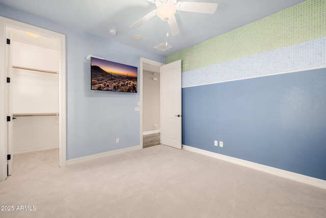 unfurnished bedroom featuring light carpet, ceiling fan, a walk in closet, and baseboards