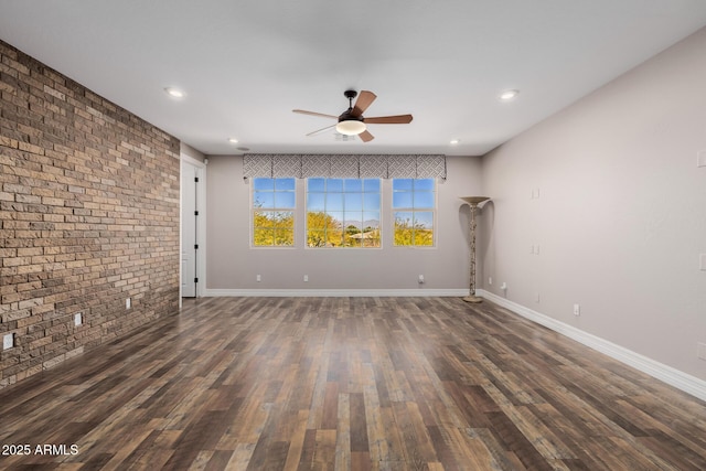 spare room featuring brick wall, wood finished floors, and baseboards