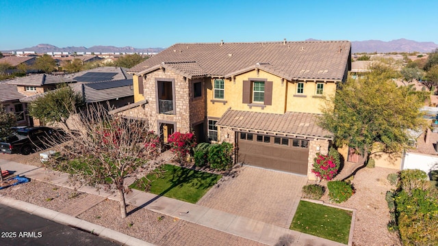 view of front facade featuring a garage, a tile roof, stone siding, decorative driveway, and stucco siding