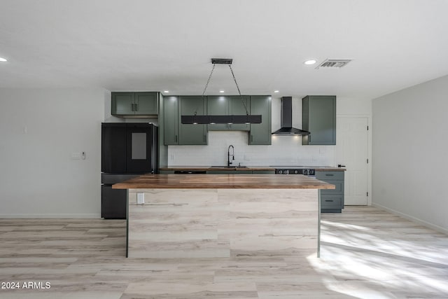 kitchen featuring pendant lighting, sink, butcher block counters, black refrigerator, and wall chimney exhaust hood