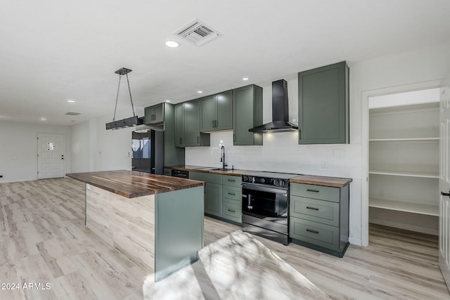 kitchen featuring black refrigerator, stainless steel electric range oven, butcher block countertops, and wall chimney range hood