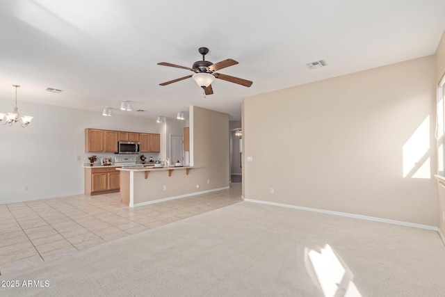 kitchen featuring ceiling fan with notable chandelier, a kitchen bar, light carpet, decorative light fixtures, and kitchen peninsula