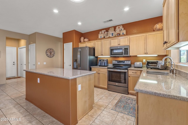 kitchen with light tile patterned floors, light brown cabinets, a kitchen island, stainless steel appliances, and light stone countertops