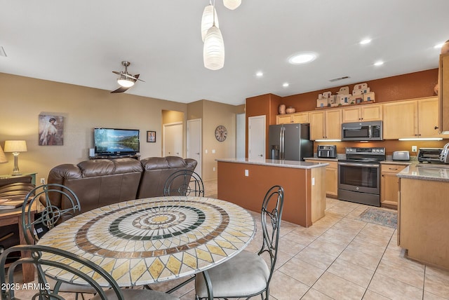 kitchen with appliances with stainless steel finishes, a center island, light tile patterned floors, light stone countertops, and light brown cabinets