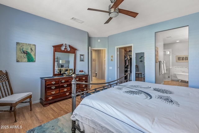 bedroom featuring connected bathroom, a walk in closet, light wood-type flooring, a closet, and ceiling fan