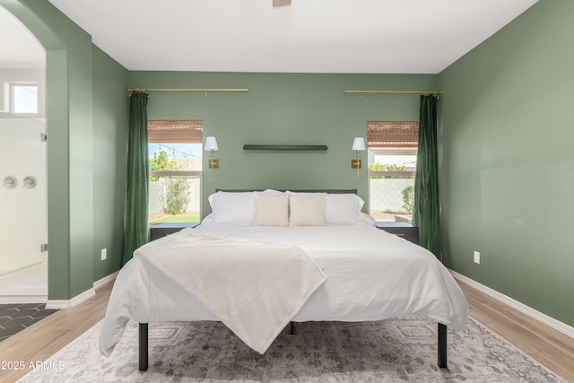 bedroom with multiple windows, wood finished floors, and baseboards