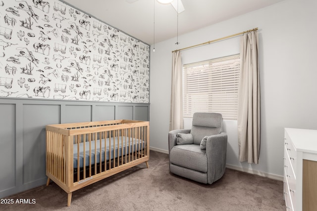 carpeted bedroom featuring a crib, a wainscoted wall, and a decorative wall