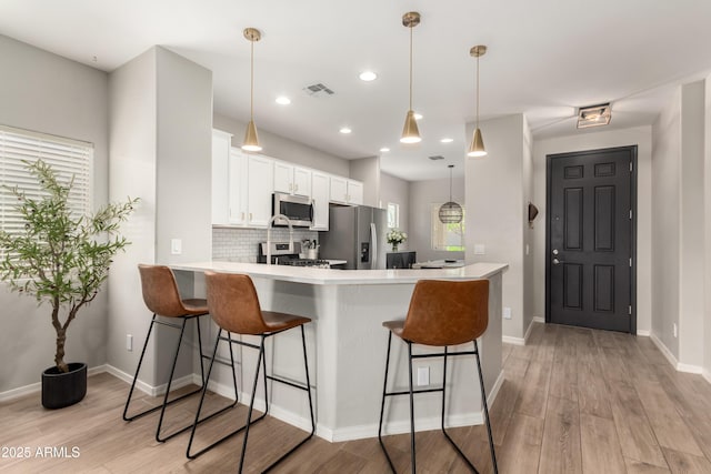 kitchen with visible vents, a peninsula, stainless steel appliances, light wood-style floors, and white cabinetry