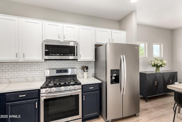 kitchen with tasteful backsplash, white cabinets, light stone countertops, stainless steel appliances, and light wood-style floors