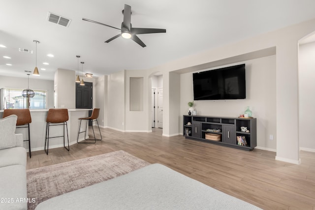 living area featuring arched walkways, light wood-type flooring, and visible vents