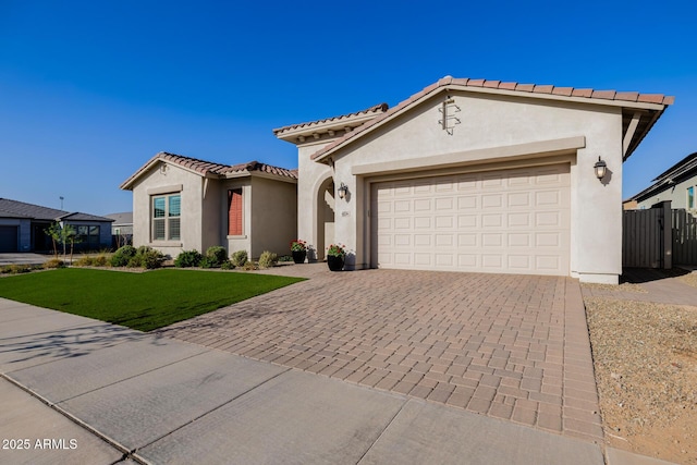 mediterranean / spanish-style home featuring a tile roof, decorative driveway, a front lawn, and stucco siding