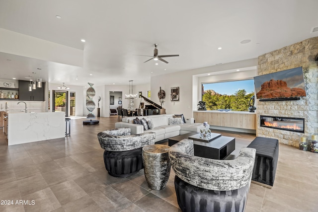 living room with ceiling fan with notable chandelier and a stone fireplace