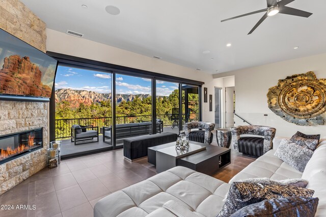 tiled living room with ceiling fan and a stone fireplace