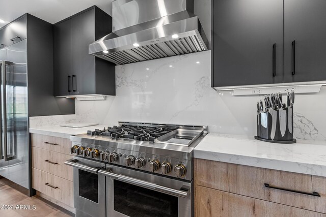 kitchen with range with two ovens, light stone countertops, decorative backsplash, and wall chimney range hood