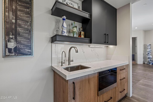 kitchen with sink, light stone countertops, backsplash, and hardwood / wood-style flooring