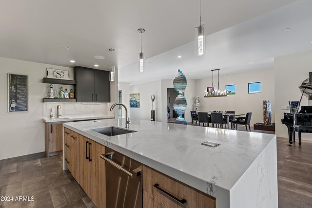 kitchen with light stone counters, an island with sink, sink, and hanging light fixtures