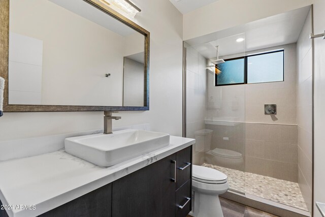 bathroom with toilet, a tile shower, and vanity