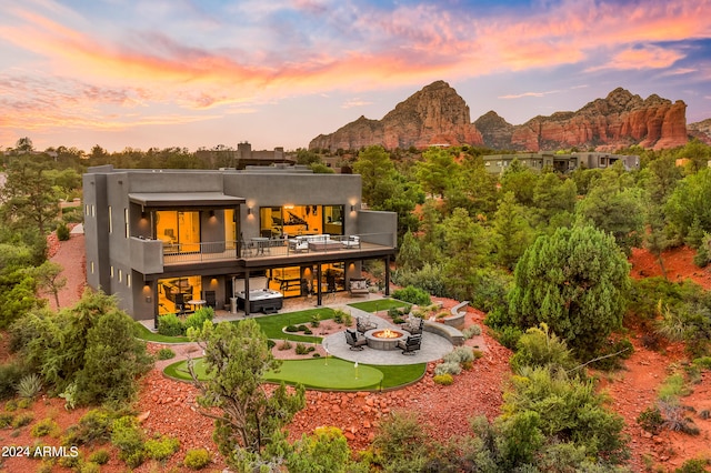 back house at dusk featuring a mountain view, a patio area, an outdoor fire pit, and a balcony