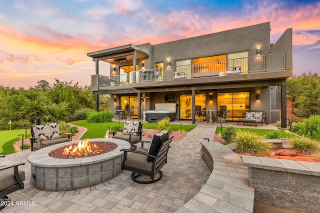 back house at dusk with a balcony, a patio area, and an outdoor living space with a fire pit