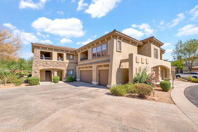 mediterranean / spanish house with stucco siding, driveway, stone siding, an attached garage, and a balcony