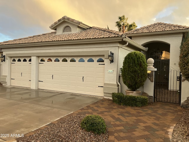 mediterranean / spanish-style house with a tiled roof, stucco siding, driveway, an attached garage, and a gate