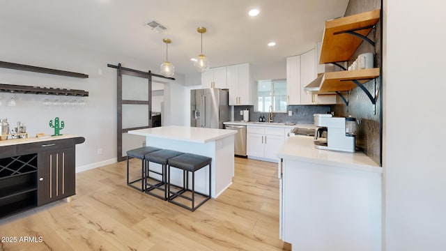 kitchen with pendant lighting, white cabinetry, stainless steel appliances, a center island, and a barn door