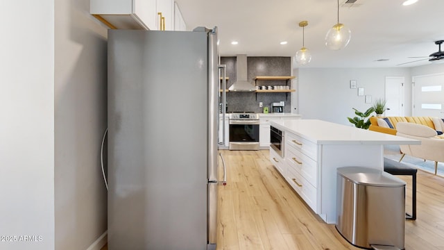 kitchen featuring hanging light fixtures, white cabinetry, appliances with stainless steel finishes, and wall chimney range hood