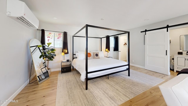 bedroom with light hardwood / wood-style flooring, a wall unit AC, and a barn door