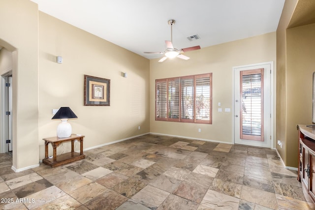 entryway with arched walkways, a ceiling fan, visible vents, baseboards, and stone finish flooring