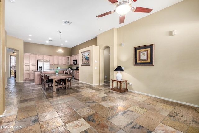 dining room with arched walkways, stone tile flooring, visible vents, ceiling fan, and baseboards