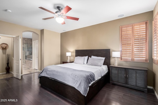 bedroom featuring arched walkways, ceiling fan, connected bathroom, dark wood-type flooring, and baseboards