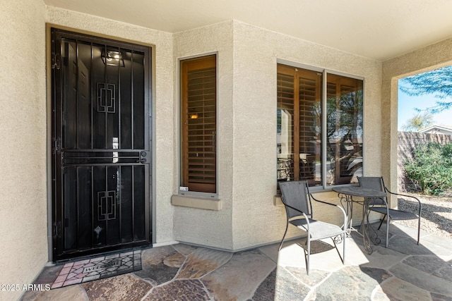 view of exterior entry with a patio, fence, and stucco siding